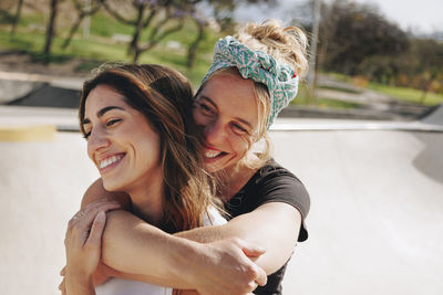 Smiling woman embracing friend from behind on sunny day