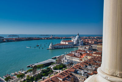 High angle view of cityscape by sea against clear blue sky