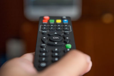Cropped hand of person holding remote control while watching tv