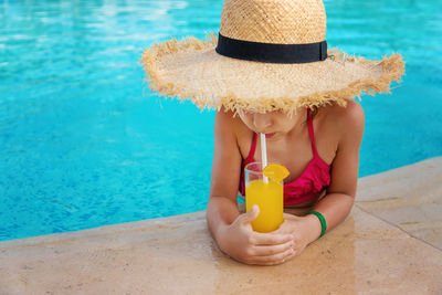 Girl in straw hat drinking orange juice at pool side