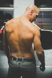 Rear view of shirtless muscular man leaning on wall in parking lot