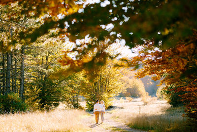 Rear view of woman standing amidst trees on field