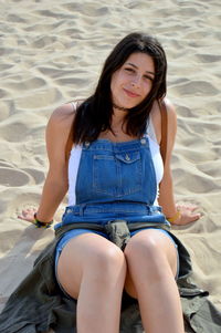 Portrait of beautiful young woman sitting on sandy beach