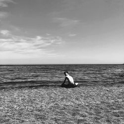 Woman sitting on beach against sky