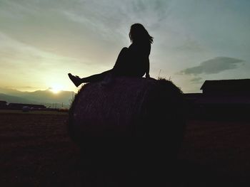 Silhouette man sitting on field against sky during sunset