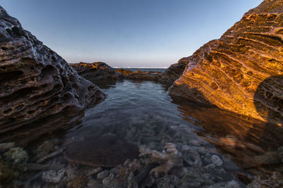 Rock formations by sea against clear sky