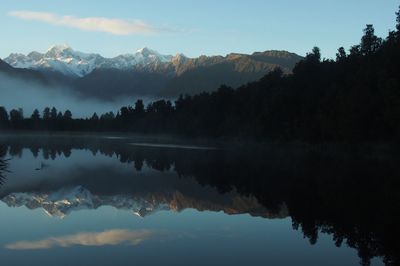 Reflection of silhouette trees in lake against sky