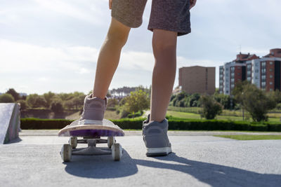 Close up of legs of a kid on a skateboard about to start enjoying a skateboarders park in his city. 