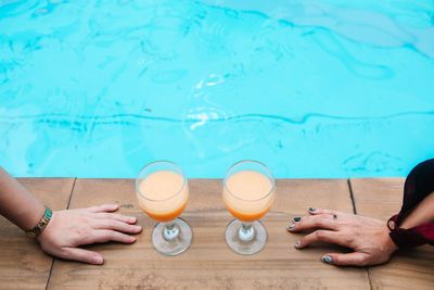 Cropped hands of women by juice against swimming pool