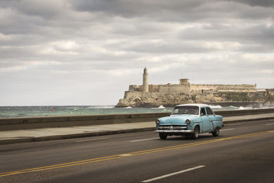 Cars on road by sea against sky in city