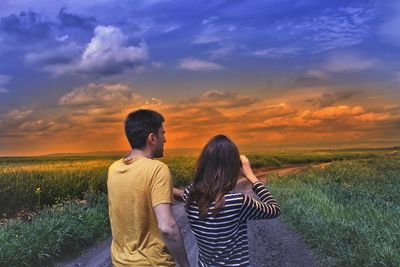 Couple on road amidst field against sky during sunset