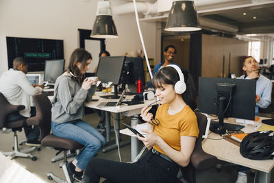 Female it professional using digital tablet while coworkers working in background at creative office