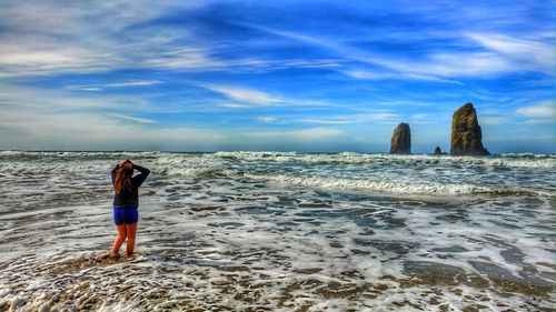 Rear view of woman standing on beach against sky