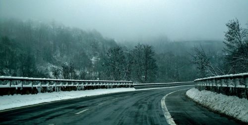 Road by snow covered trees against sky