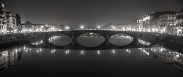 Illuminated bridge over river in city against clear sky at night