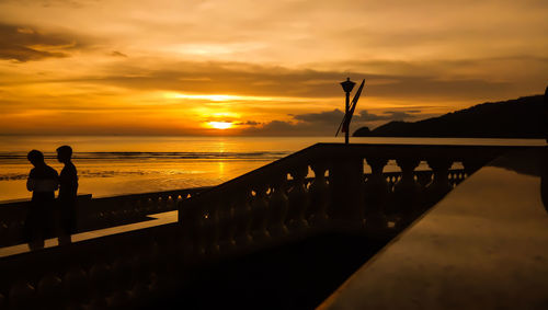 Silhouette people standing by railing against sea during sunset