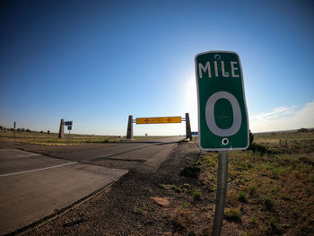 Road sign on field against clear blue sky