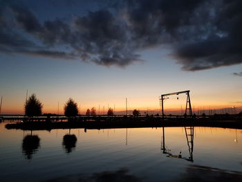 Silhouette cranes by trees against sky during sunset