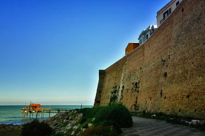 Building by sea against clear blue sky