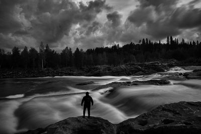 Rear view of man standing on rock against sky