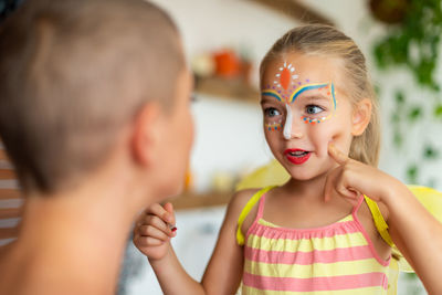 Smiling mother and daughter with face paint sitting at home