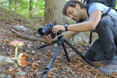 Side view of man photographing mushrooms in forest