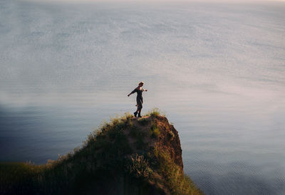 Rear view of man standing on rock by sea against sky