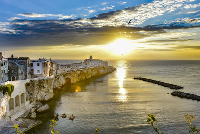 High angle view of buildings by sea against sky during sunset