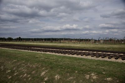 View of railroad tracks on field against cloudy sky