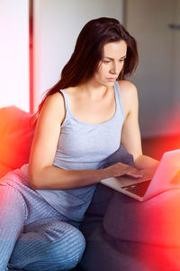 Young woman using mobile phone while sitting on sofa at home