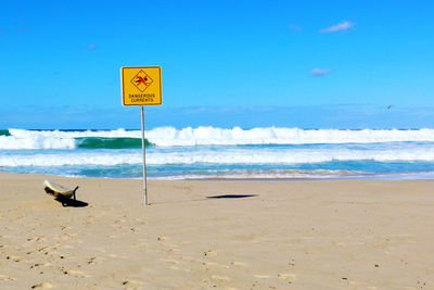 Warning sign on beach against sky