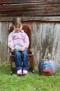 Full length of girl sitting on chair by pumpkin during halloween