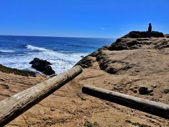 Scenic view of sea with man standing on rock against clear sky