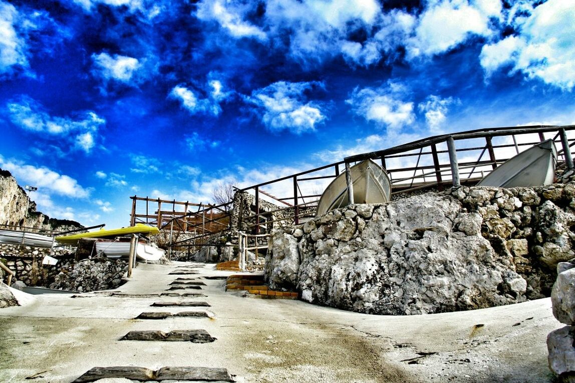 sky, the way forward, built structure, architecture, cloud - sky, cloud, railing, diminishing perspective, connection, blue, day, sunlight, rock - object, long, transportation, bridge - man made structure, cloudy, outdoors, vanishing point, low angle view