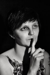 Mid adult tattooed woman with finger on lips against black background