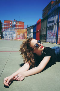 Woman in sunglasses lying down on footpath against sky