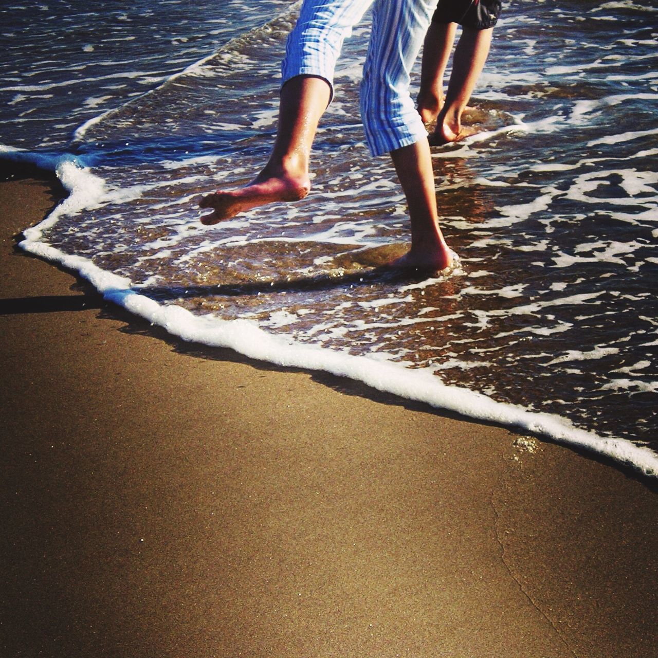 low section, water, person, lifestyles, beach, leisure activity, shore, sand, surf, motion, wave, standing, barefoot, human foot, high angle view, sea, walking, vacations