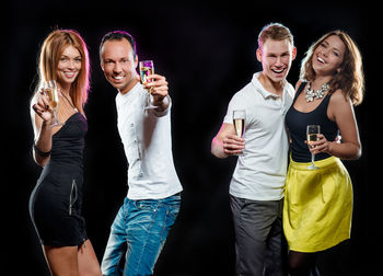 Friends holding champagne flutes while standing against black background