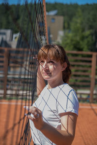 Young woman looking away while standing by net