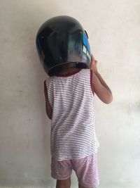 Rear view of boy wearing crash helmet while standing against wall