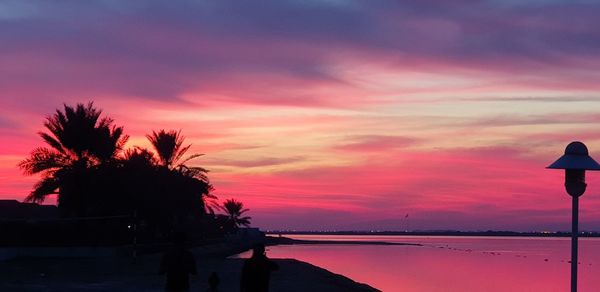 Silhouette trees by sea against romantic sky at sunset