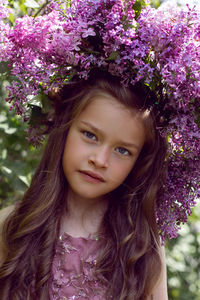 Caucasian girl child seven years old in a purple dress stands in nature with a wreath of lilacs