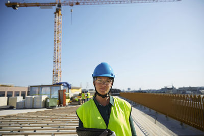 Confident female engineer in reflective clothing with digital tablet at construction site against clear sky