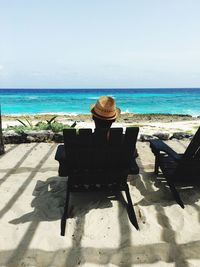 Rear view of man sitting on lounge chair at beach against sky