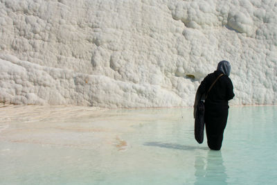 Woman wearing burka walking in water at beach against rock formation