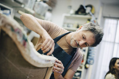 Mature craftsperson stitching furniture in workshop