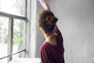 Woman looking away while standing against window