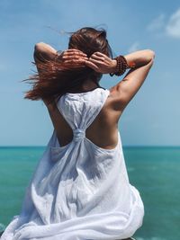 Rear view of woman holding hair while sitting against turquoise sea