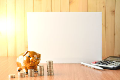 Coins stacked by piggy bank and paper on table