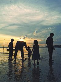 Silhouette people at beach against sky during sunset